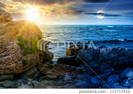 weekend on a rocky beach at the sea. day and night time change concept. beautiful coastline on summer solstice. seascape scenery with clouds above horizon with sun and moon at twilight. mysterious weekend on a rocky beach at the sea. day and night time change concept. beautiful coastline on summer solstice. seascape scenery with clouds above horizon with sun and moon at twilight. mysterious 131717410