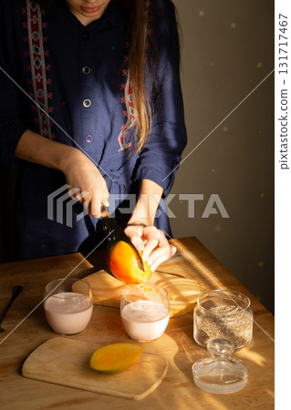 Girl slicing fresh mango on wooden board with chia seeds and yogurt drinks 131717467