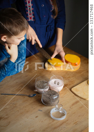 Brother watching sister slice fresh mango for chia pudding Brother watching sister slice fresh mango for chia pudding 131717468