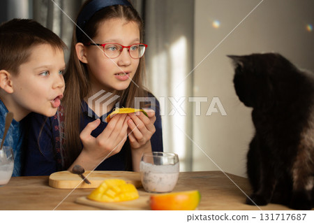 Children talk to black cat with fresh mango slice 131717687