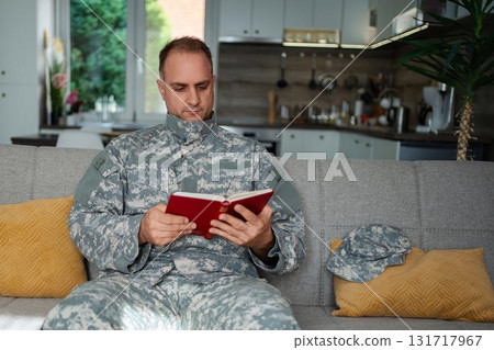Soldier reading a book sitting on the sofa at home Soldier reading a book sitting on the sofa at home 131717967