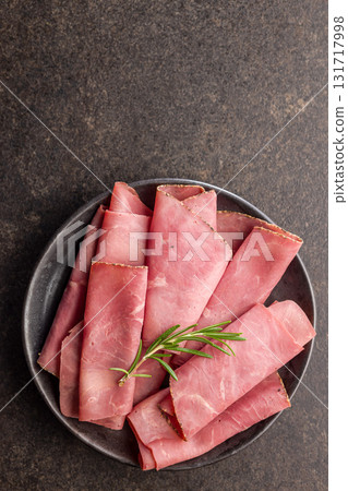 Sliced beef pastrami on plate on black table. Top view. 131717998