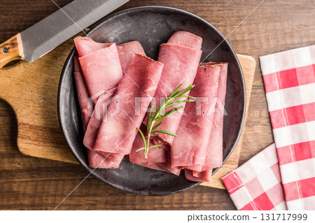 Sliced beef pastrami on plate on wooden table. Top view. 131717999