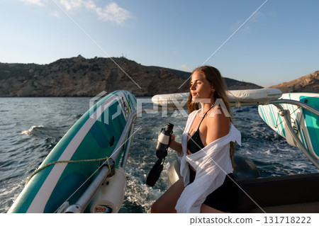 Woman, boat, ocean: young woman holding binoculars, cruising calm sea near mountains at sunset. 131718222
