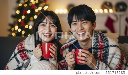 Couples snuggle under a blanket in front of a fireplace, drinking hot cocoa 131718285