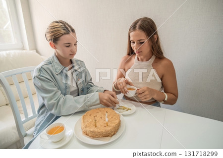 Cake Sharing Friends Tea Party: Two women enjoy tea and cake together indoors, likely celebrating or bonding. 131718299