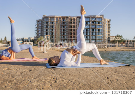 Yoga Beach Women Fitness - Two women practice yoga poses on a sandy beach in front of a building. 131718307