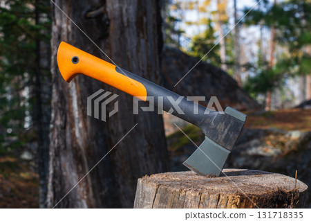 Tourist ax on a stump in a summer forest. Chopping wood with an ax. Tourist camping. Summer day. The concept of adventure and freedom. 131718335