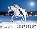 A woman in a white dress galloping on a white horse on a snowy moonlit night 131718397