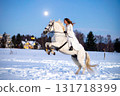 A woman in a white dress jumping on a white horse on a snowy moonlit night 131718399
