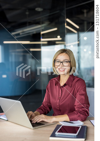Smiling businesswoman in a modern office, confidently typing on a laptop at her desk, projecting professionalism and success while working remotely or in corporate leadership roles 131718604