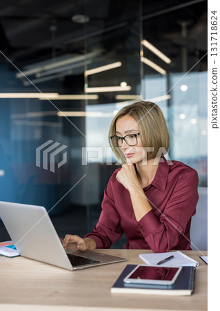 Businesswoman with glasses collaborating and concentrating at her modern office workspace, using a laptop and other digital devices to manage her business tasks efficiently Businesswoman with glasses collaborating and concentrating at her modern office workspace, using a laptop and other digital devices to manage her business tasks efficiently 131718624