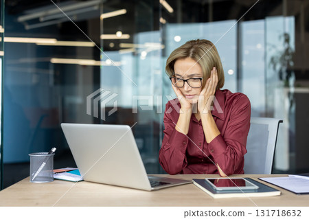 Stressed businesswoman touching her face with both hands, staring at the laptop screen while sitting at a desk in a modern office, overwhelmed by work pressures and deadlines Stressed businesswoman touching her face with both hands, staring at the laptop screen while sitting at a desk in a modern office, overwhelmed by work pressures and deadlines 131718632