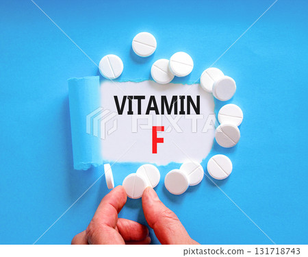 Vitamin F symbol. Concept words Vitamin F on beautiful white paper. White pills tablets. Doctor's hand. Beautiful blue background. Medical healthy lifestyle Vitamin F concept. 131718743