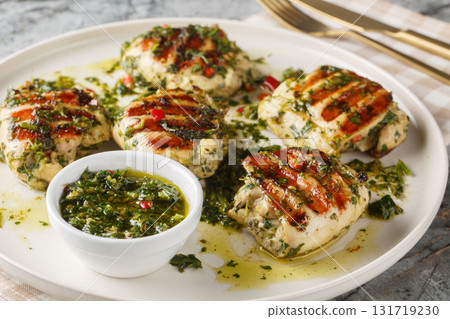 Grilled chimichurri chicken thighs with garlic, herbs and vegetable oil close-up in a plate. Horizontal Grilled chimichurri chicken thighs with garlic, herbs and vegetable oil close-up in a plate. Horizontal 131719230