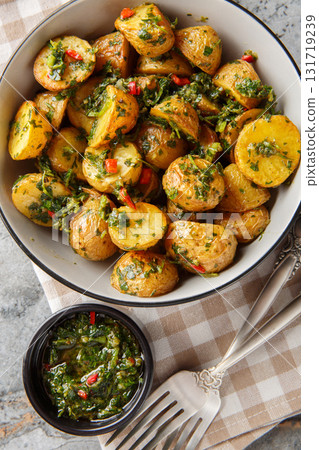 Golden roasted potatoes are tossed with a bright and peppery chimichurri sauce closeup on the plate on the table. Vertical top view Golden roasted potatoes are tossed with a bright and peppery chimichurri sauce closeup on the plate on the table. Vertical top view 131719239