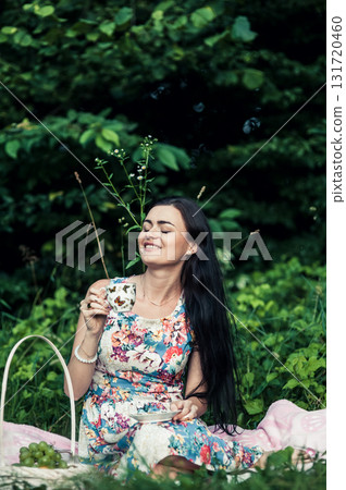 A lady in a floral dress sits on a blanket in the grass A lady in a floral dress sits on a blanket in the grass 131720460