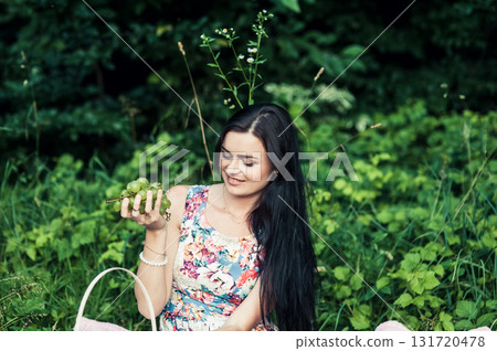 A beautiful girl at a picnic in the forest with grapes in her hands A beautiful girl at a picnic in the forest with grapes in her hands 131720478