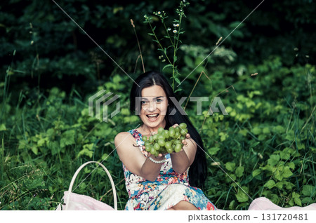 A beautiful woman relaxes at a picnic in the forest with grapes in her hands A beautiful woman relaxes at a picnic in the forest with grapes in her hands 131720481