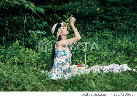 A young girl at a picnic in the park holds a large bunch of grapes against a backdrop of green trees A young girl at a picnic in the park holds a large bunch of grapes against a backdrop of green trees 131720505