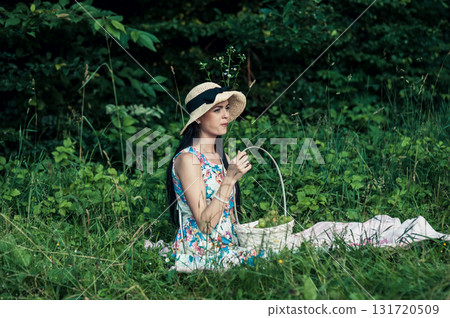 A beautiful woman relaxes at a picnic in the forest with grapes in her hands A beautiful woman relaxes at a picnic in the forest with grapes in her hands 131720509