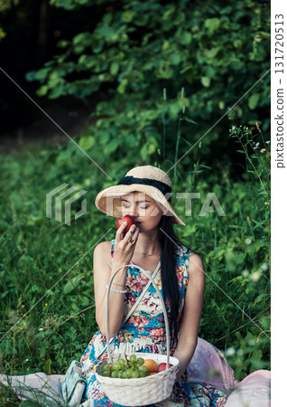 A beautiful girl at a picnic wearing a cute hat is holding a red nectarine 131720513
