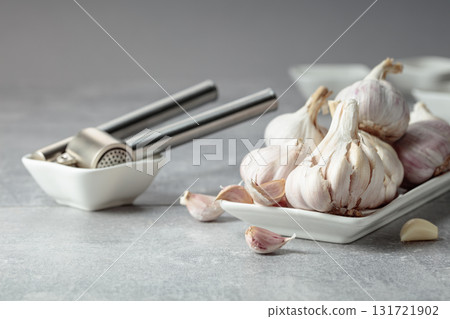 Garlic and garlic press on a grey table. 131721902