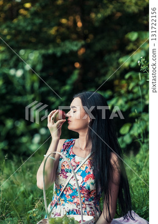 A woman in a bright floral dress sits on a soft pink rug at a picnic 131722156
