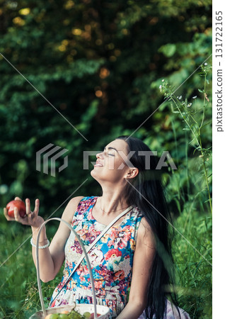 A lady in a light floral dress sits on a pink rug surrounded by nature 131722165