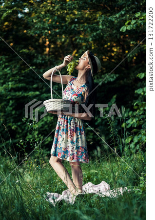A young girl stands on green grass next to a pink picnic blanket 131722200