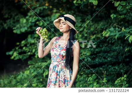 A young girl stands on the grass with a bunch of green grapes A young girl stands on the grass with a bunch of green grapes 131722224