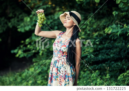 A young girl stands on the grass with a bunch of green grapes A young girl stands on the grass with a bunch of green grapes 131722225