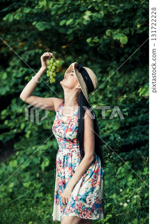 A woman in a floral dress holds a bunch of grapes 131722228