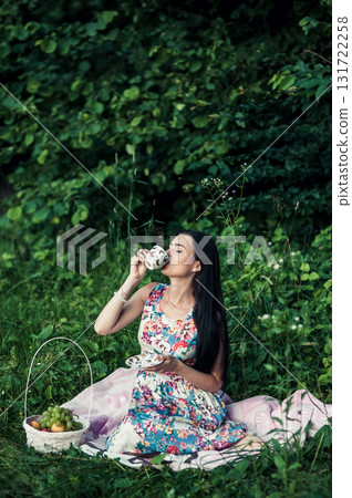 A woman in a floral outfit holds a cup of aromatic coffee at a picnic 131722258