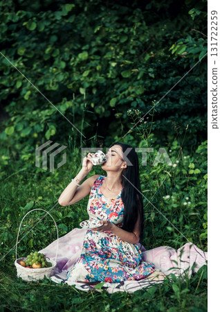 A young girl sits among the greenery of the forest with a cup of tea in her hands A young girl sits among the greenery of the forest with a cup of tea in her hands 131722259