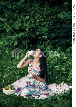 A young girl sits among the greenery of the forest with a cup of tea in her hands A young girl sits among the greenery of the forest with a cup of tea in her hands 131722261