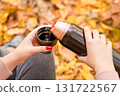 Female hands holding a thermos of hot tea against the background autumn leaves 131722567