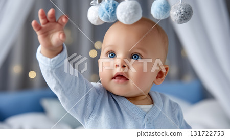 Baby reaching for soft pom poms hanging from mobile in a beautifully decorated nursery. Calm and welcoming atmosphere with gently lit background. Concept of childcare, parenting, nursery design. 131722753