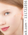 Half face portrait of a funny smiling young girl applying serum on face using an dropper. Gen Alpha. Blonde Caucasian girl with blue eyes studio shot. Advertising concept skin care for teenagers 131722856