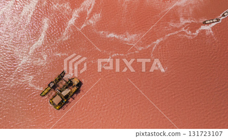Aerial view of a salt harvesting barge on the pink saline lake near Santa Pola and Torrevieja in Spain, showing vivid water color and salt patterns under summer sunlight 131723107
