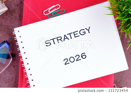 A notepad displays the word strategy and the year 2026 on a desk with office supplies, suggesting a focus on future planning and business endeavors A notepad displays the word strategy and the year 2026 on a desk with office supplies, suggesting a focus on future planning and business endeavors 131723454