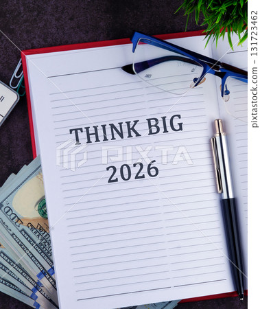 A notebook is open to a page with THINK BIG and 2026 printed, alongside a pen, eyeglasses, and a stack of money, suggesting financial planning 131723462