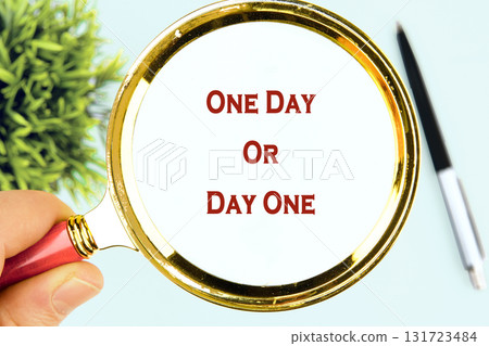A hand holds a magnifying glass over the words One Day Or Day One, next to a pen and small plant on a bright table, inviting reflection on future choices A hand holds a magnifying glass over the words One Day Or Day One, next to a pen and small plant on a bright table, inviting reflection on future choices 131723484