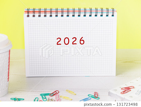A 2026 calendar sits on a desk next to a coffee cup, notebook, and paper clips. The scene focuses on business and financial preparations for the coming years 131723498