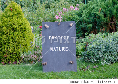 A slate sign with PROTECT NATURE is propped in a lush garden on a sunny day. The sign is adorned with rope and is urging a concept of environmental awareness and finance 131723614
