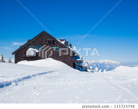 Winter scenery with a mountain hut on the summit of a snowy mountain and Mount Myoko in the distance (Yokoteyama, Shiga Kogen, Nagano Prefecture) 131723748