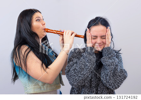 two attractive teenager girls having fun with wooden flute isolated on light background 131724192