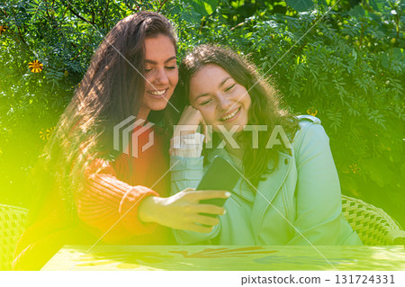 two women with smartphone  sit in outdoor cafe, sharing the news and  laughing, girls party concept 131724331