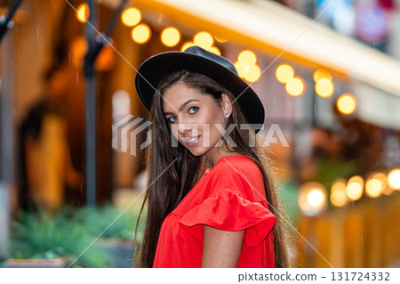 elegant young woman in a red dress and a black hat on a background of street cafe lights 131724332