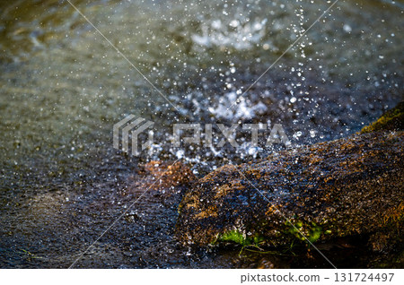 close-up view of water splashing over a rock in a pool under a fountain 131724497